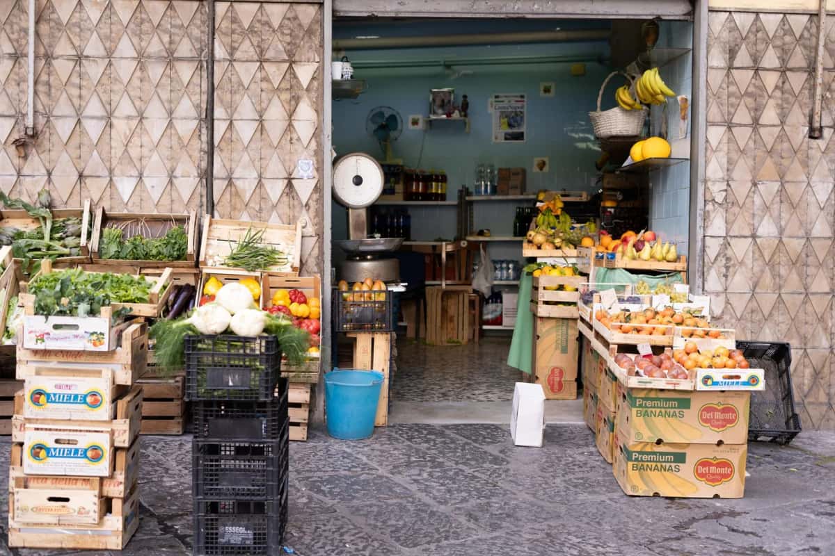 Étal de fruits et légumes d'un primeur de quartier à Naples, cageots de tomates, artichauts et agrumes posés sur le trottoir, en Italie