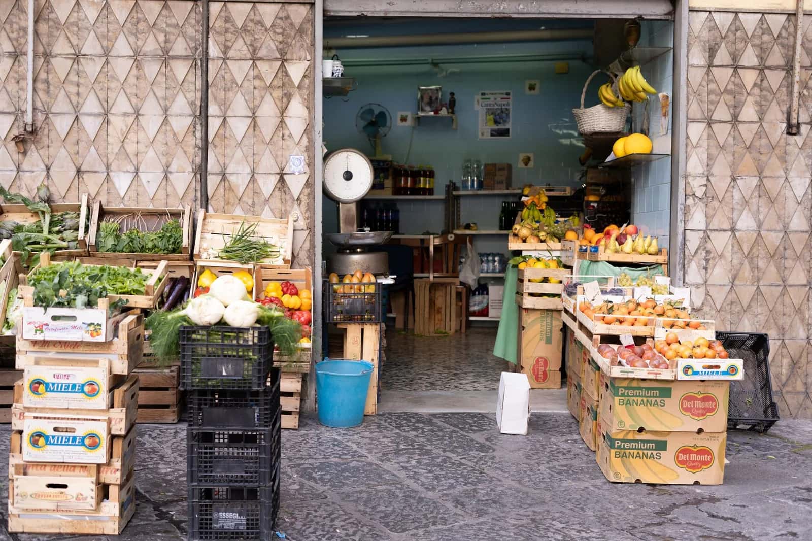 Étal de fruits et légumes d'un primeur de quartier à Naples, cageots de tomates, artichauts et agrumes posés sur le trottoir, en Italie