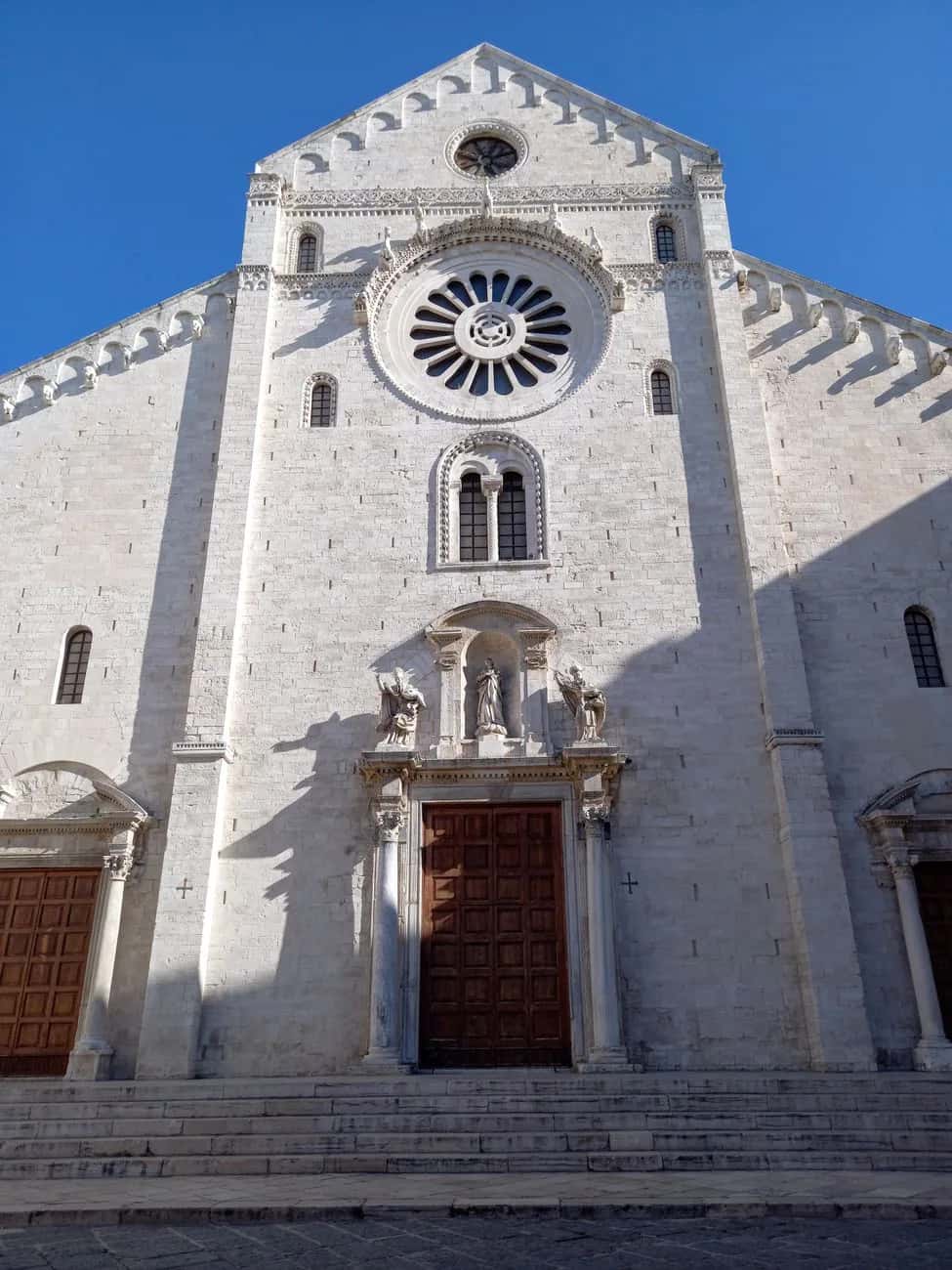 Façade romane en pierre claire de la basilique Saint-Nicolas à Bari, avec sa rosace, son portail sculpté et ses arcatures
