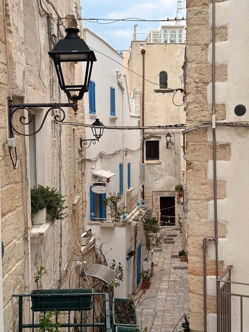 Ruelle étroite de Bari Vecchia, avec ses murs en pierre, ses lampadaires en fer forgé et ses volets bleus