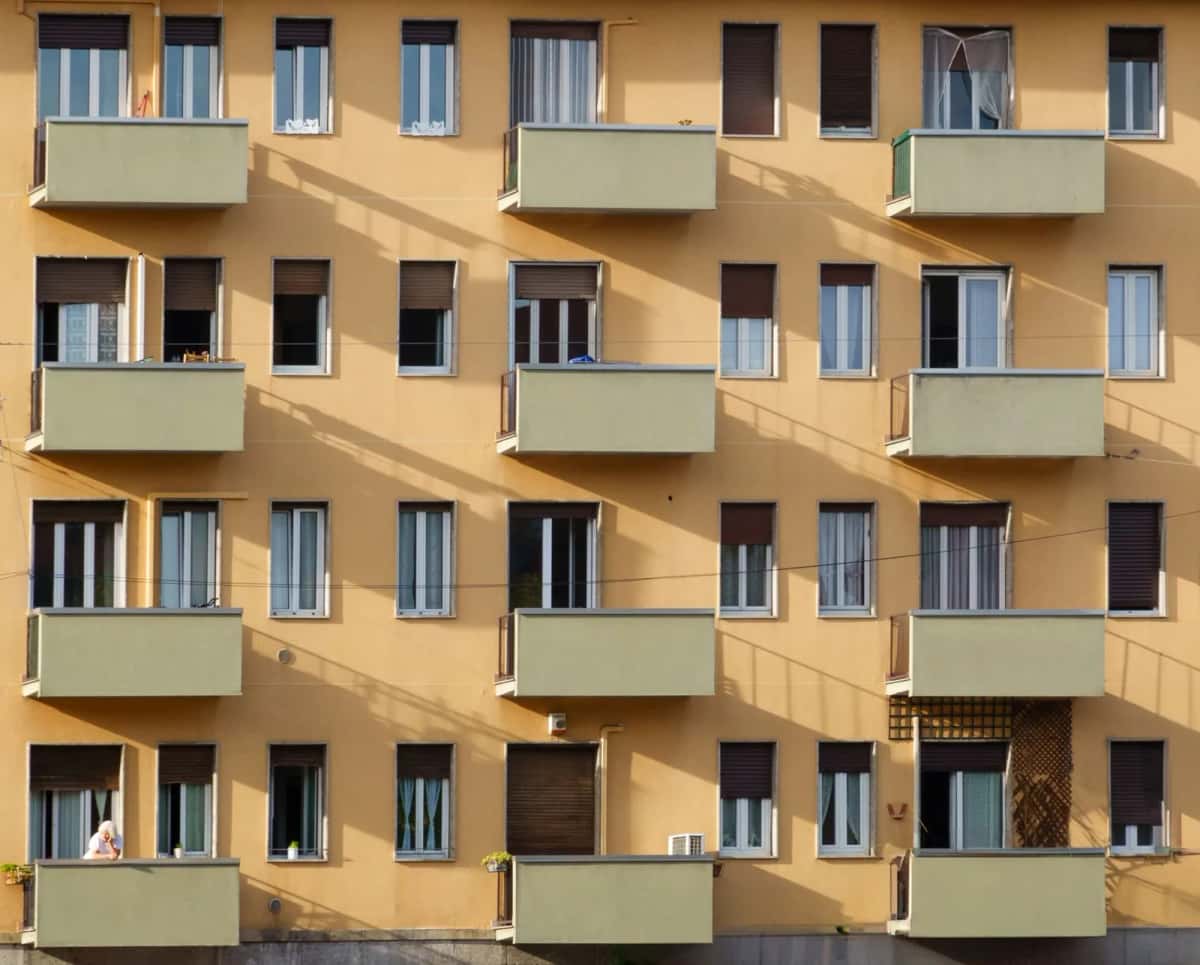 Façade ocre d'un immeuble d'habitation italien avec ses balcons en enfilade et ses persiennes, éclairée par le soleil de fin de journée