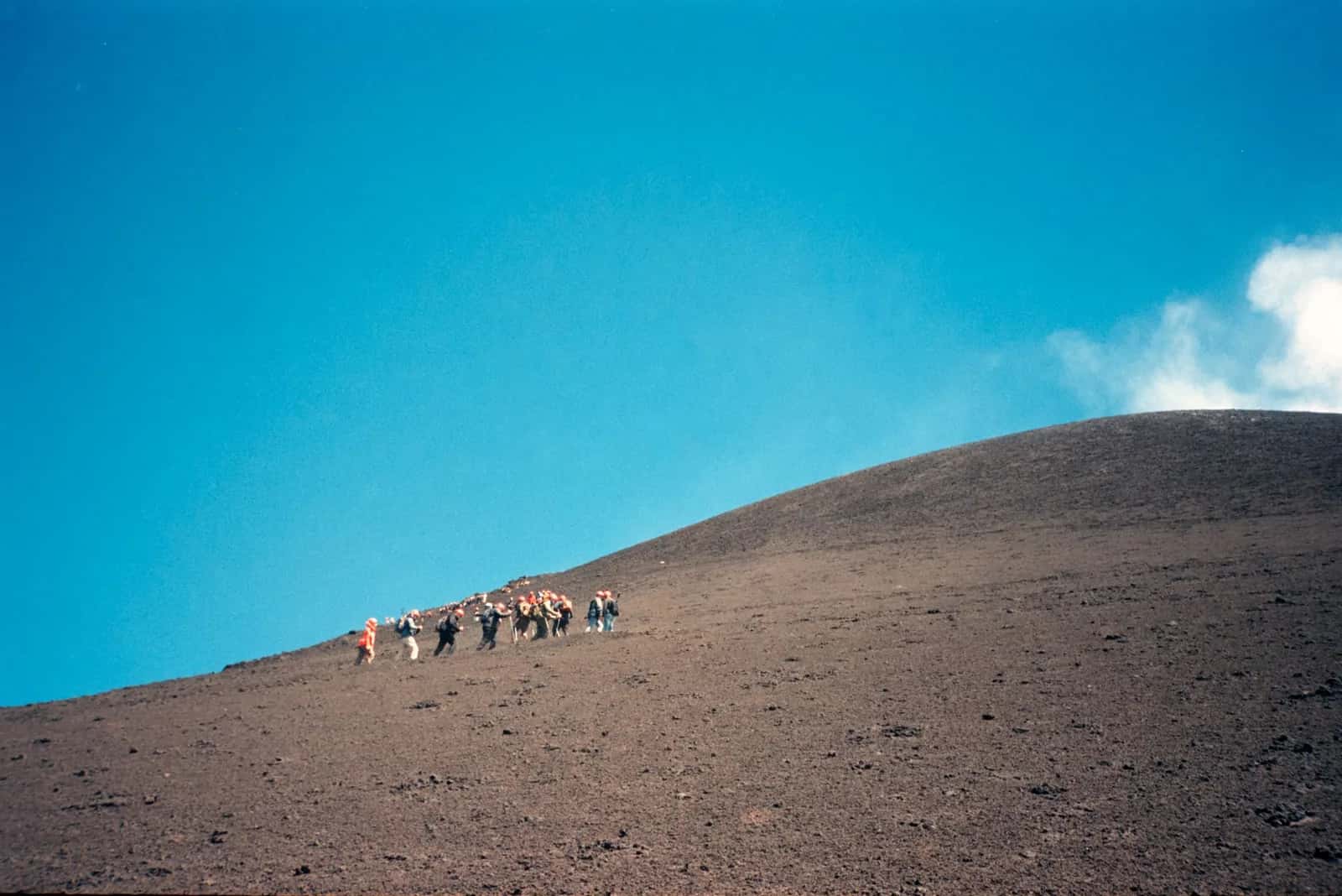 Groupe de randonneurs gravissant la pente de cendre noire près des cratères sommitaux de l'Etna, en Sicile