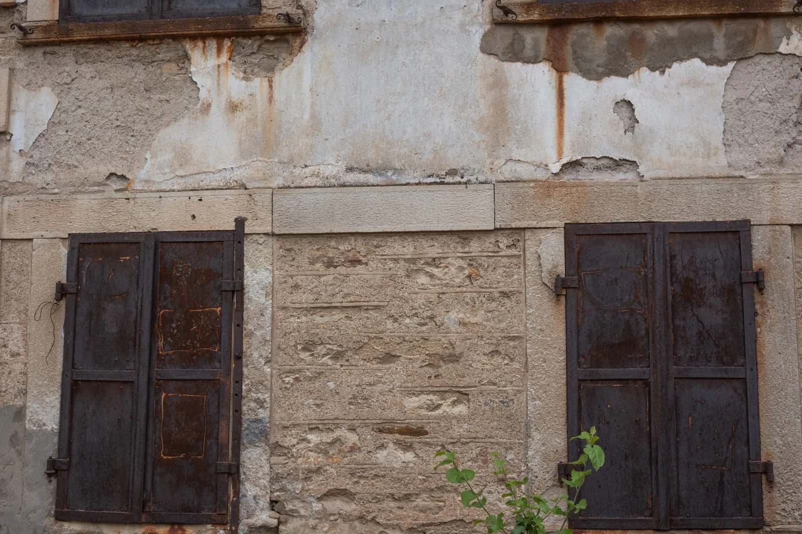 Façade en pierre abîmée aux volets rouillés d'une vieille maison à rénover