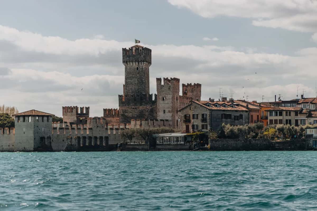 Le château Scaliger de Sirmione vu depuis le lac de Garde, avec ses remparts crénelés et l'eau turquoise, en Italie