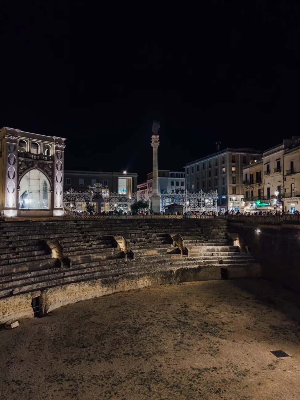 Gradins de l'amphithéâtre romain de Lecce, de nuit, avec la colonne de Sant'Oronzo et le Sedile sur la Piazza Sant'Oronzo