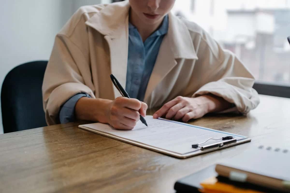 Personne remplissant un formulaire administratif sur un bureau, comme le kit postale de demande de permesso di soggiorno en Italie