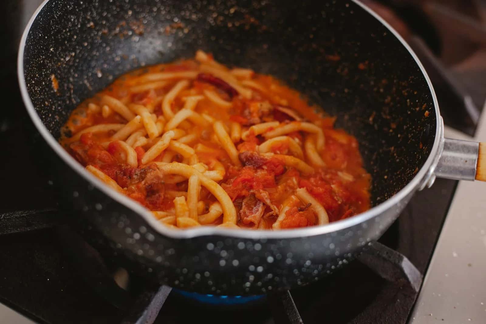 Pâtes à l'amatriciana dans une poêle, sauce tomate et morceaux de guanciale