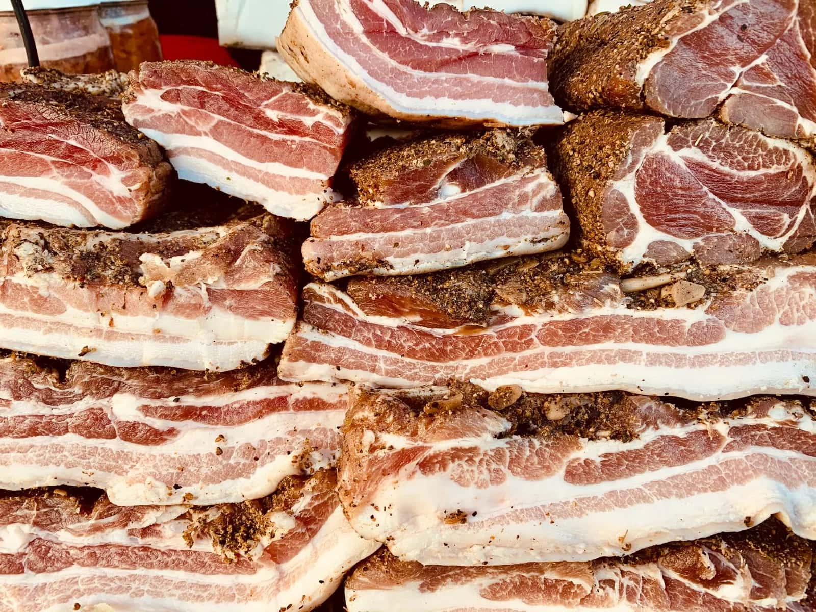 Larges tranches de lard de porc poivré avec leur bande de gras blanc, proche du guanciale