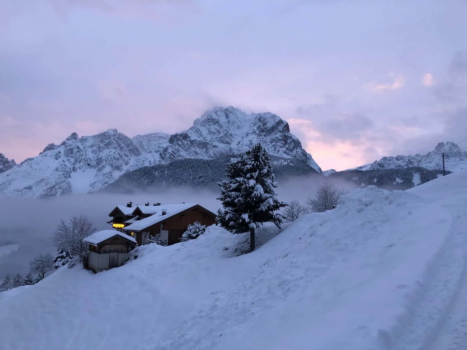 Chalets sous la neige au crépuscule, avec les sommets des Dolomites en arrière-plan