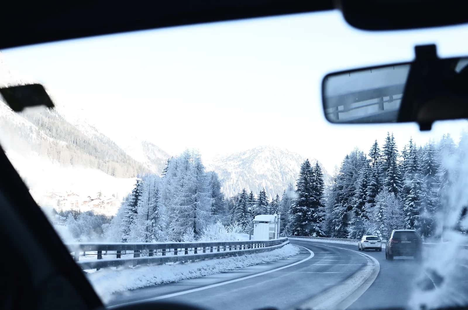 Route de montagne enneigée vue depuis une voiture, entre sapins givrés et versants blancs des Alpes
