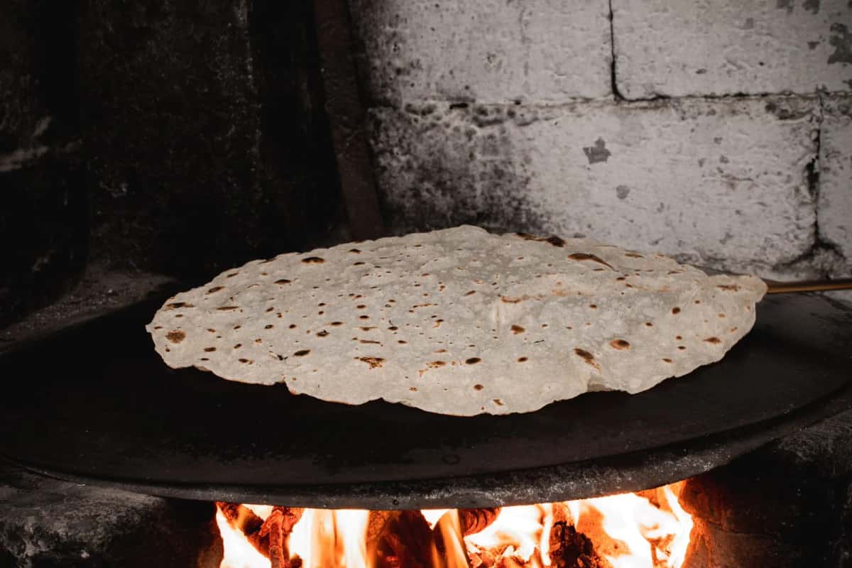 Grande feuille de pain plat en cuisson sur une plaque au-dessus des braises, à la manière du pane carasau sarde