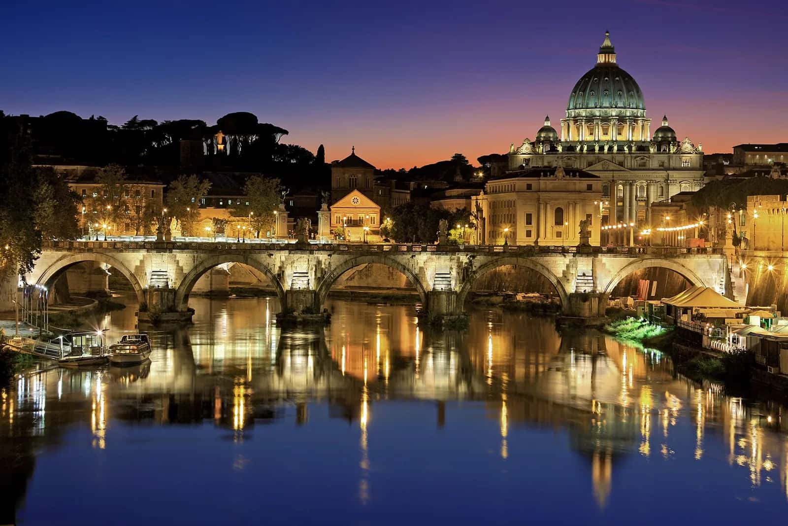La coupole illuminée de la basilique Saint-Pierre derrière le pont Saint-Ange, au crépuscule, à Rome